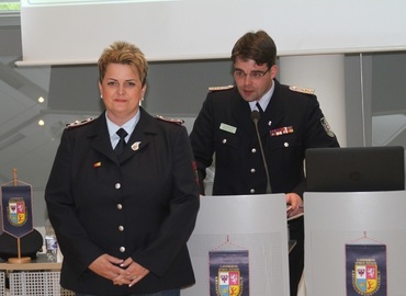 Robert Buder (Hintergrund) verliest die Urkunde zu Auszeichnung der ehemaligen Schatzmeisterin der Kreis­jugend­feuerwehr Spree-Neiße