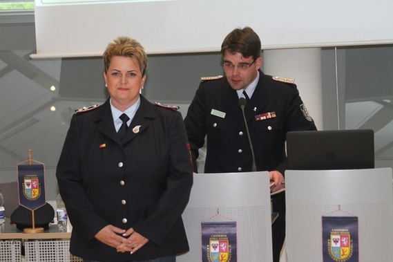Robert Buder (Hintergrund) verliest die Urkunde zu Auszeichnung der ehemaligen Schatzmeisterin der Kreis­jugend­feuerwehr Spree-Neiße