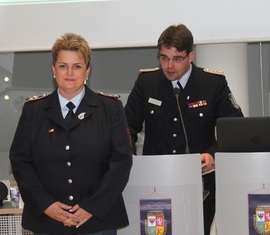 Robert Buder (Hintergrund) verliest die Urkunde zu Auszeichnung der ehemaligen Schatzmeisterin der Kreis­jugend­feuerwehr Spree-Neiße
