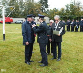 Kreis­jugend­feuerwehrwart Christian Rösiger übergibt Bernd Schulze das Ehrenzeichen der Landesjugendfeuerwehr Brandenburg in Bronze aus.