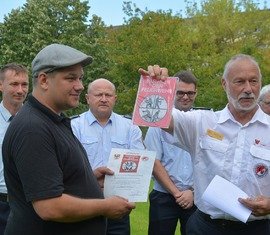 Der Präsident des Landesfeuerwehrverbandes, Rolf Fünning, überreicht das Förderschild an Geschäftsführer Sebastian Schulz