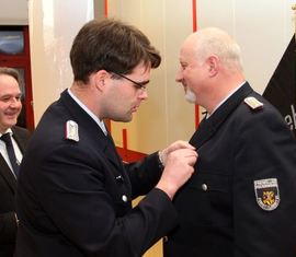 Vorsitzender des Kreis­feuerwehr­verbandes Spree-Neiß e.V. Robert Buder steckt dem ausgezeichneten Carsten Brudek das Abzeichen an die Uniformjacke.