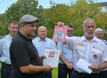 Der Präsident des Landesfeuerwehrverbandes, Rolf Fünning, überreicht das Förderschild an Geschäftsführer Sebastian Schulz