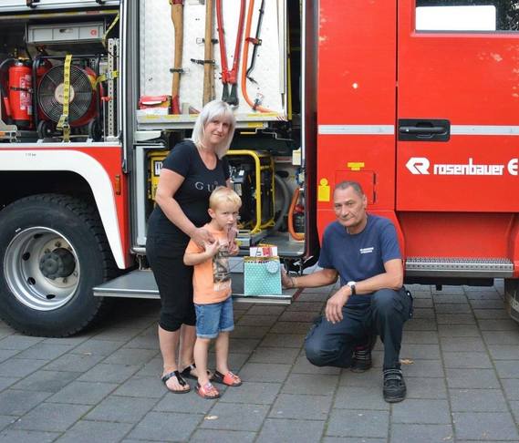 Stadtwehrführer Frank Balkow überreicht Anton Hoetzel, der von Mama Maria begleitet wird, ein kleines Dankeschön